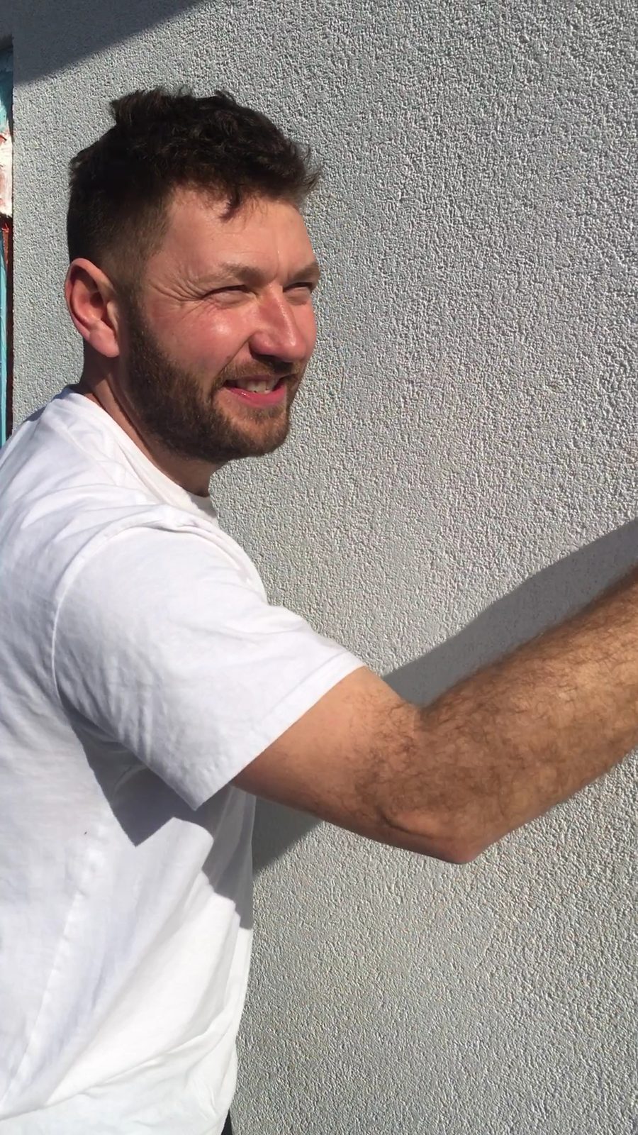 Gavin at work, smiling, with a hand on a freshly rendered wall