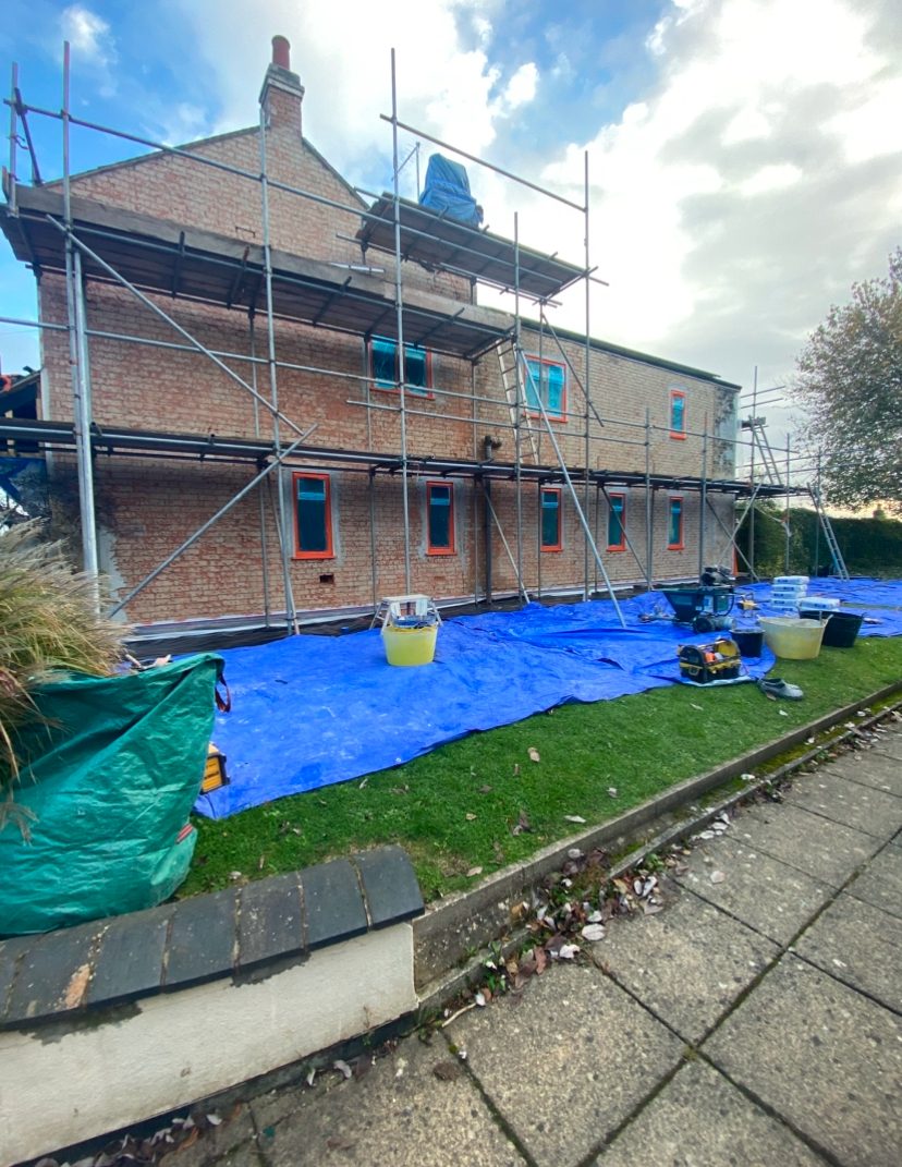 Brick house with scaffold and blue sheeting before render